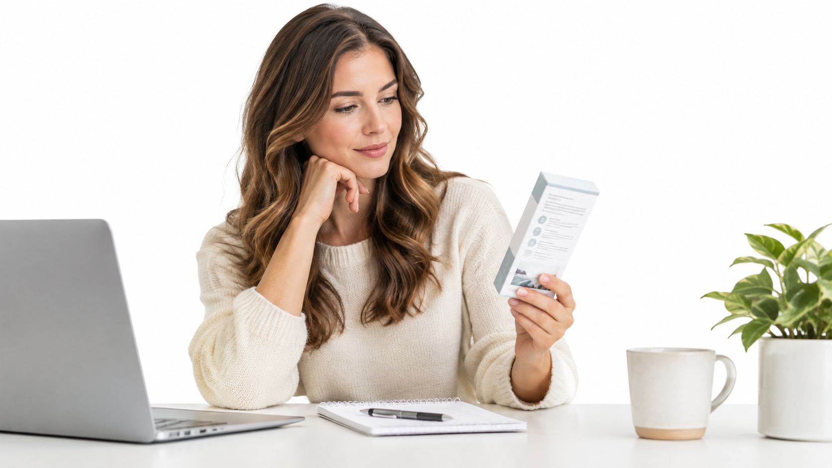A woman holding a product box while sitting at a desk with a laptop and notebook.