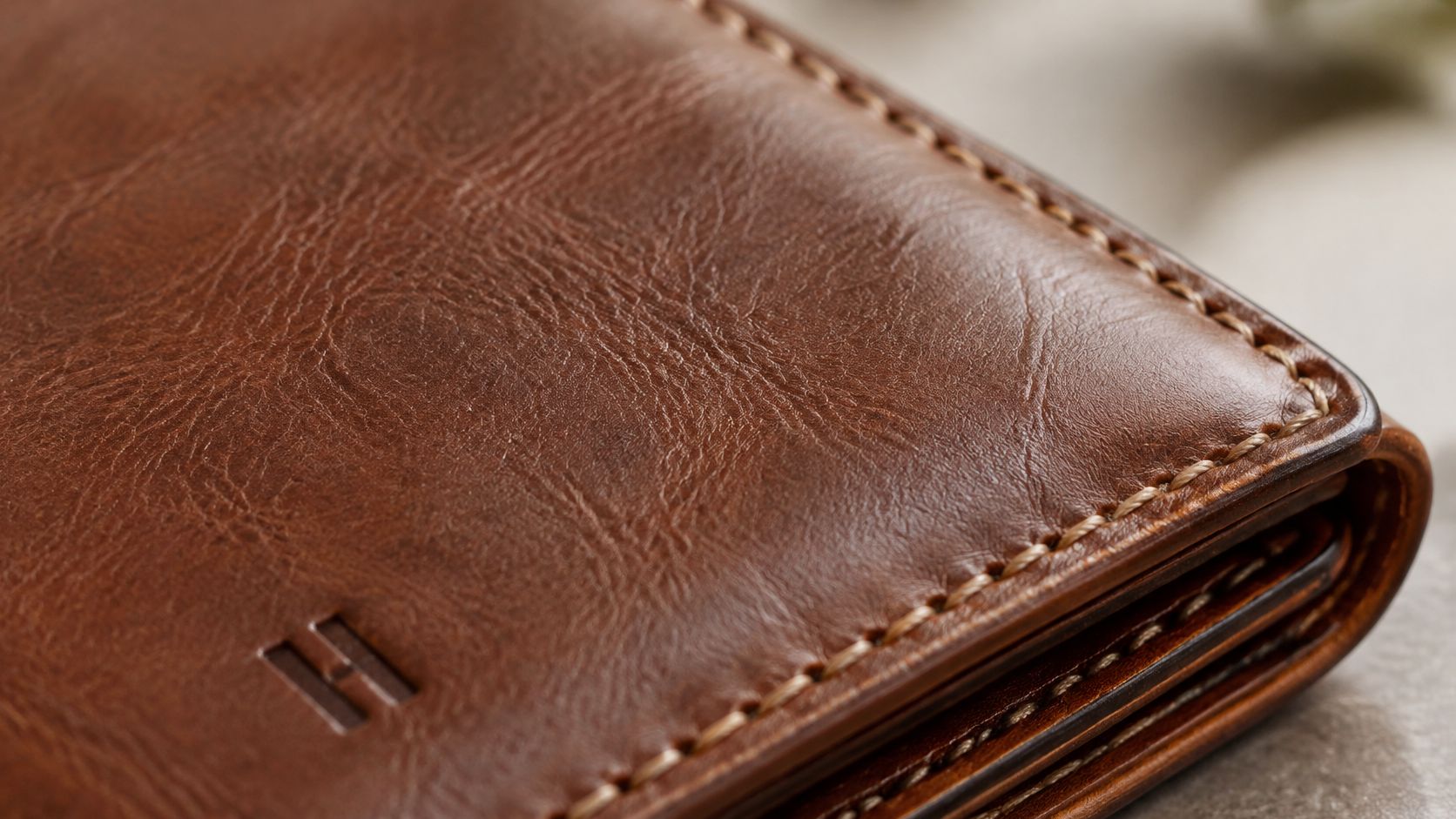A close-up of a brown leather wallet featuring detailed stitching and a small embossed letter H logo.